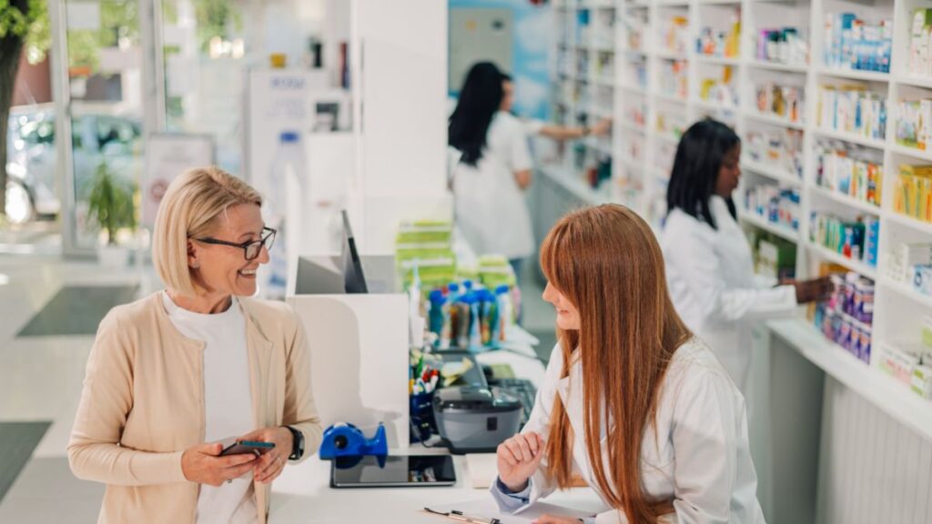 mulher-idosa-conversa-com-funcionaria-no-balcao-da-farmacia-com-outros-funcionarios-ao-fundo-shutterstock